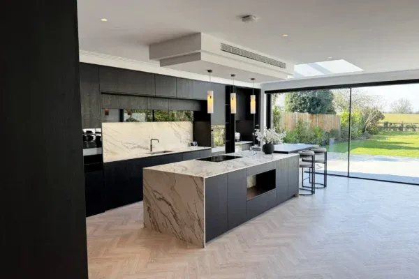 Open-plan dark kitchen with statement stone surfaces and natural wood flooring